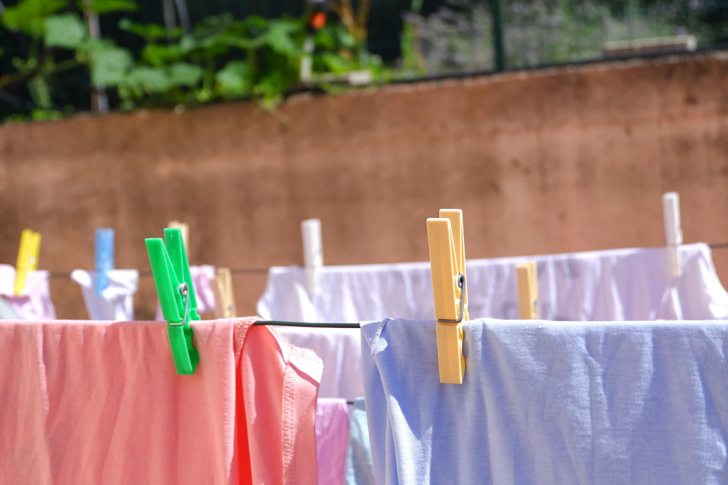 A Dagny pinafore hanging from a wooden hanger beside a white blouse