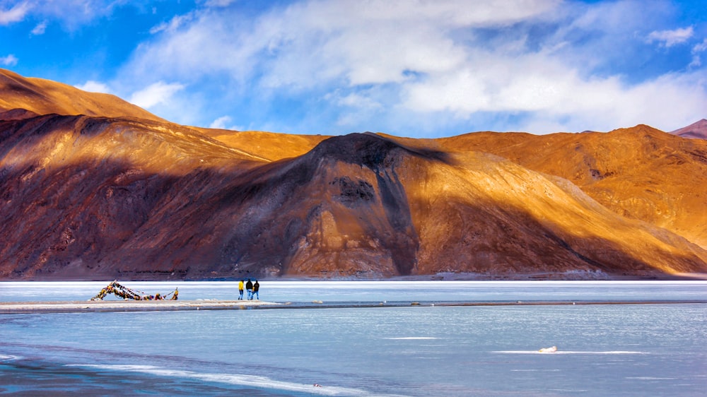 people walking on beach near brown mountain under blue sky during daytime