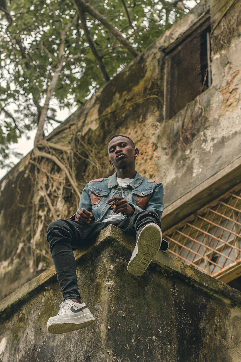 man in blue denim jacket and black pants sitting on brown concrete wall during daytime