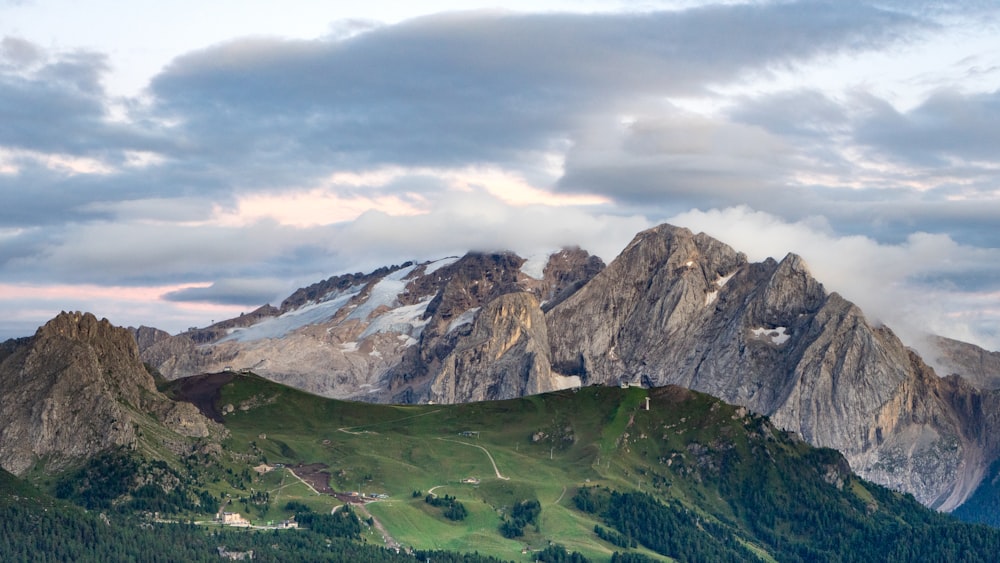 green grass field near mountain under cloudy sky during daytime