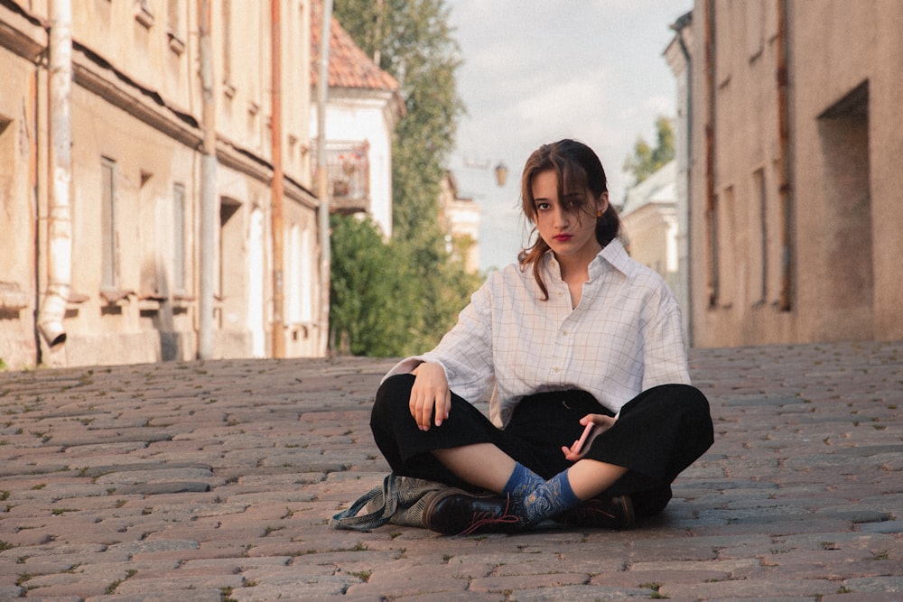 woman in white and black plaid dress shirt and black pants sitting on concrete floor during