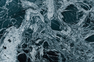 A close-up view of a natural stone slab exhibiting swirling, intricate patterns in shades of dark green and white. The marble-like surface displays a mixture of veins and speckles, creating an abstract texture.