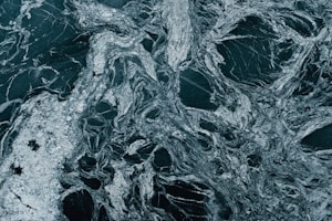 A close-up view of a natural stone slab exhibiting swirling, intricate patterns in shades of dark green and white. The marble-like surface displays a mixture of veins and speckles, creating an abstract texture.