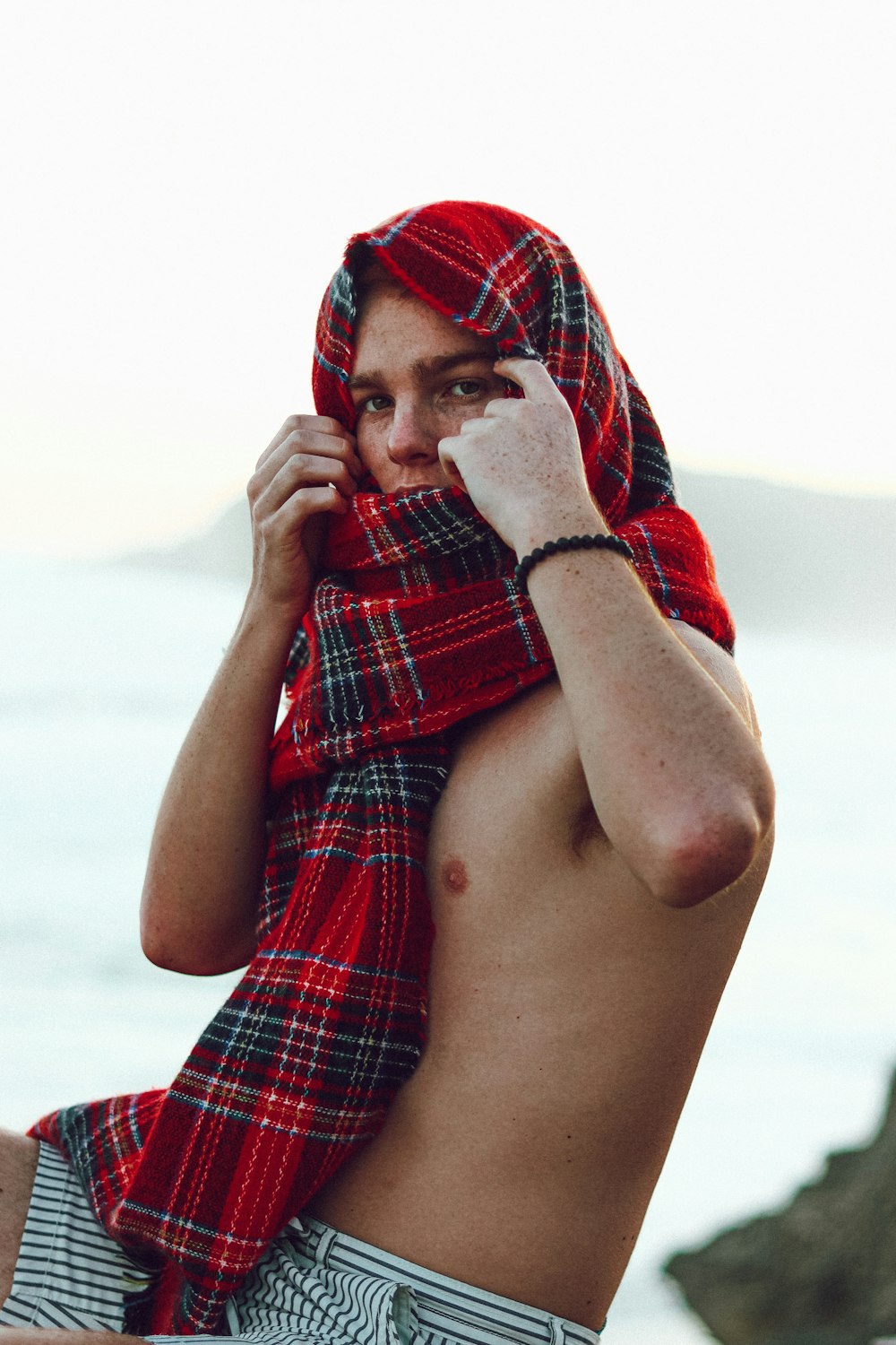 man covering his face with red and blue plaid textile