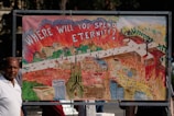 A detailed illustration depicts a scene with flames and smoke surrounding buildings, roads, and a church. The artwork features a large, bold text at the top questioning 'Where will you spend eternity?'. The imagery contrasts elements of chaos against more organized structures in a vibrant, symbolic representation.