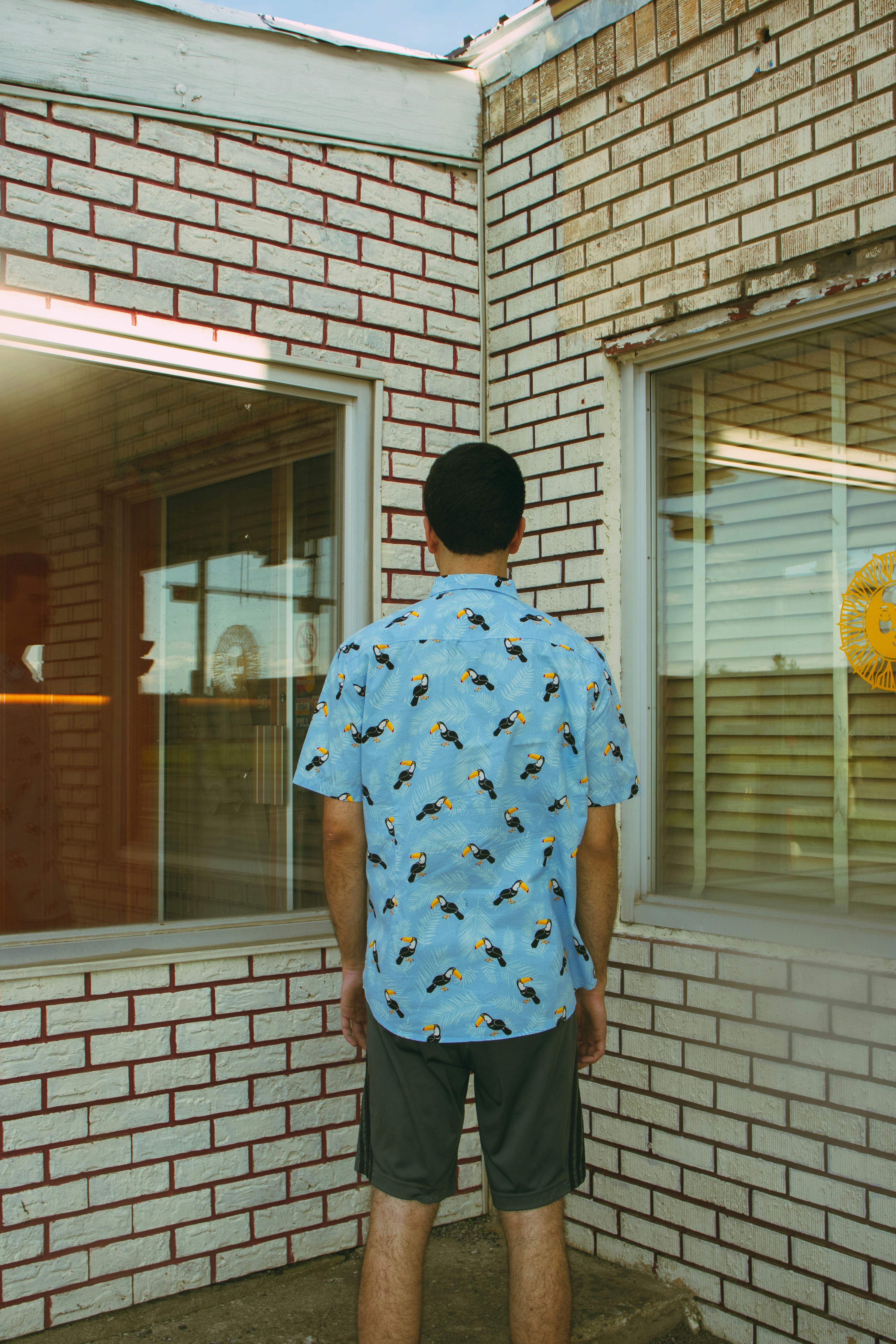 man in blue and white floral button up t-shirt standing near brown brick building during
