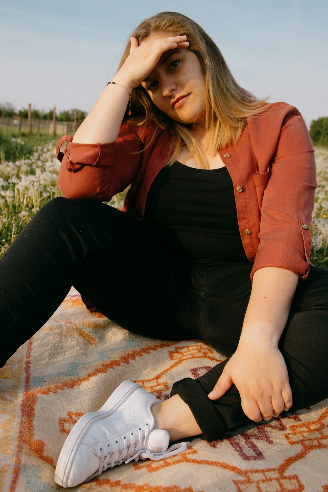 woman in brown jacket and black pants sitting on blue and white blanket