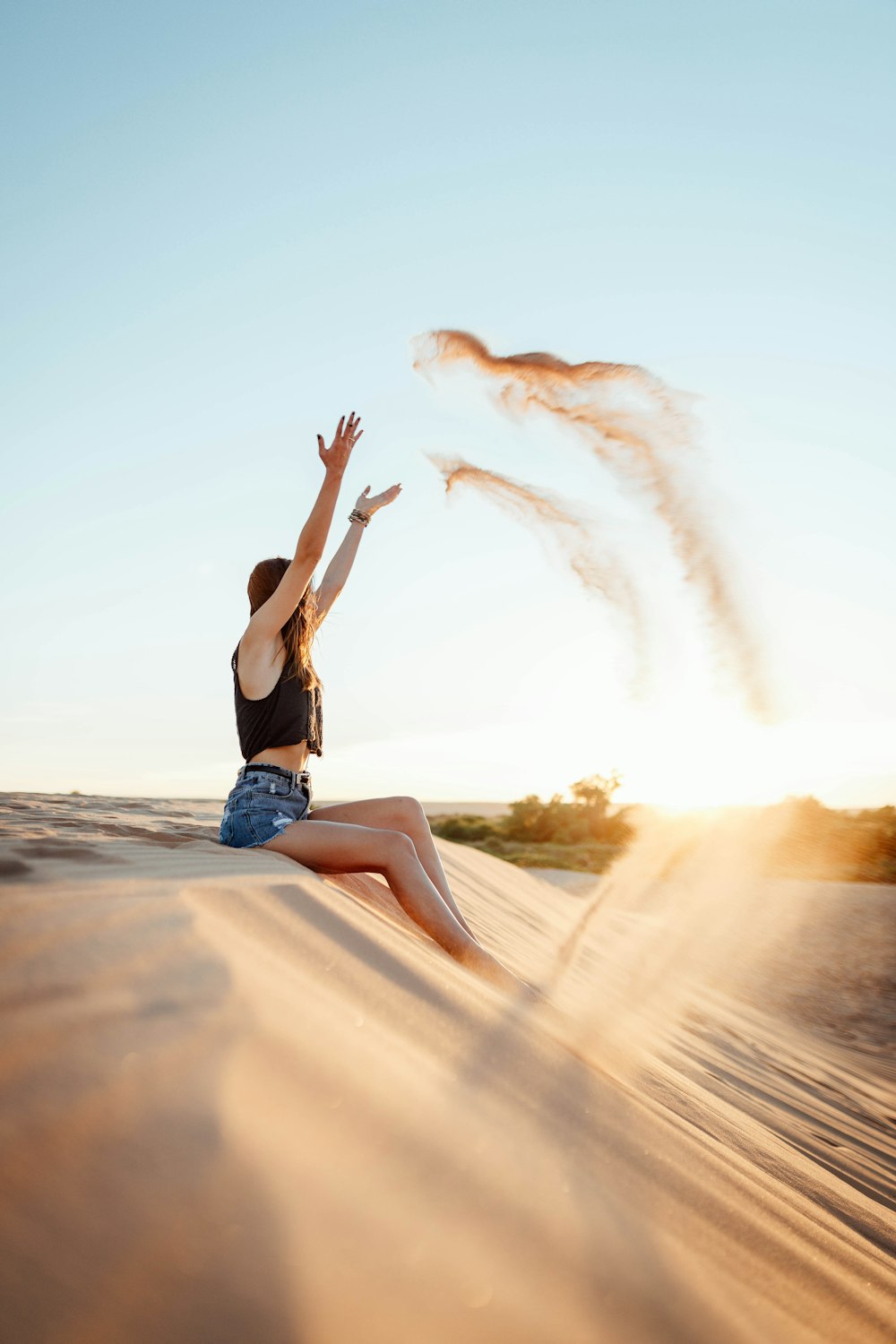 woman in black tank top and blue denim shorts jumping on brown sand during daytime