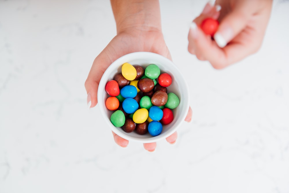 person holding white plastic cup with assorted color candies