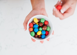 person holding white plastic cup with assorted color candies