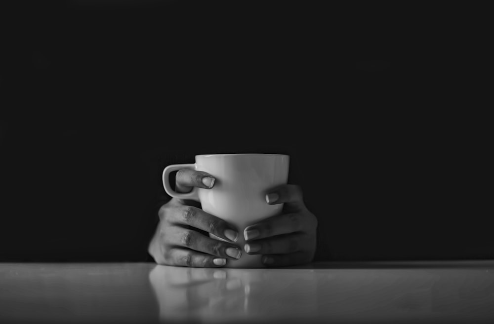 Foto en escala de grises de una persona sosteniendo una taza de cerámica