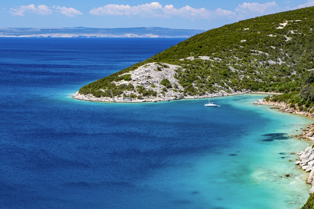 green and white mountain beside blue sea during daytime