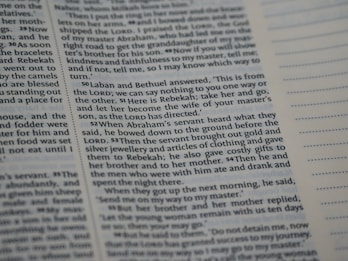 A close-up view of a page from a book with printed text in English. The passage appears to be from a religious or historical context, focusing on a dialogue involving Laban, Bethuel, and Abraham’s servant. The text is arranged in paragraphs with verse numbers in bold. Blank lined sections are visible on the opposite page.