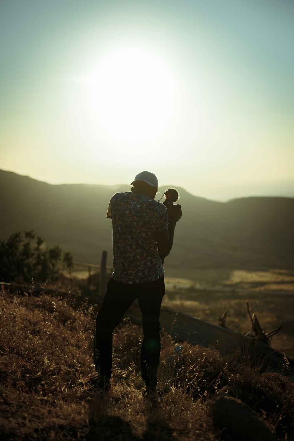 man in black and white floral shirt and black pants standing on brown field during daytime