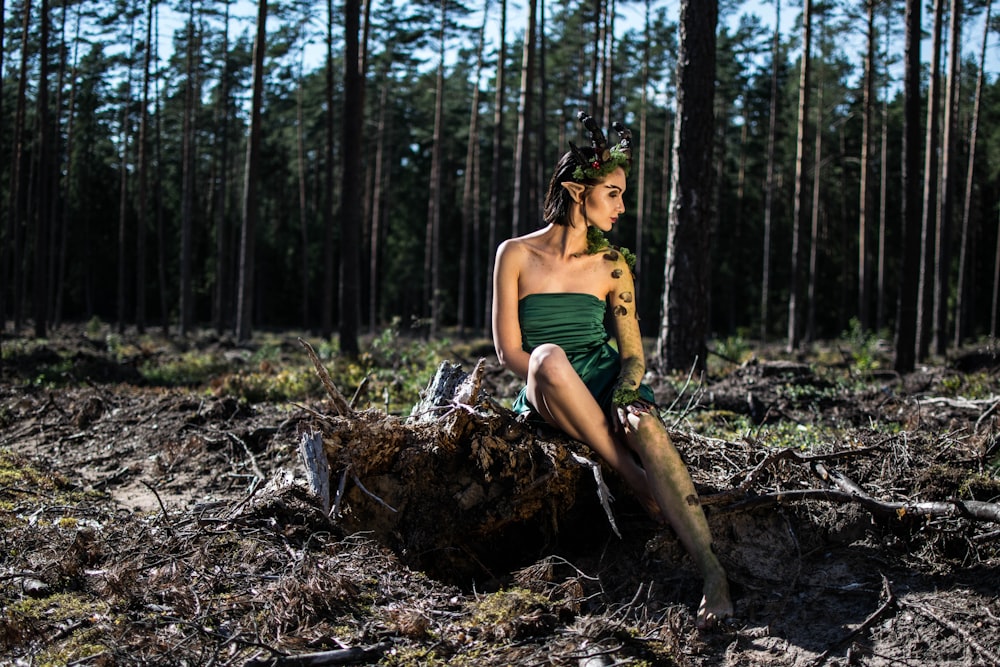 woman in green spaghetti strap dress sitting on brown tree log during daytime