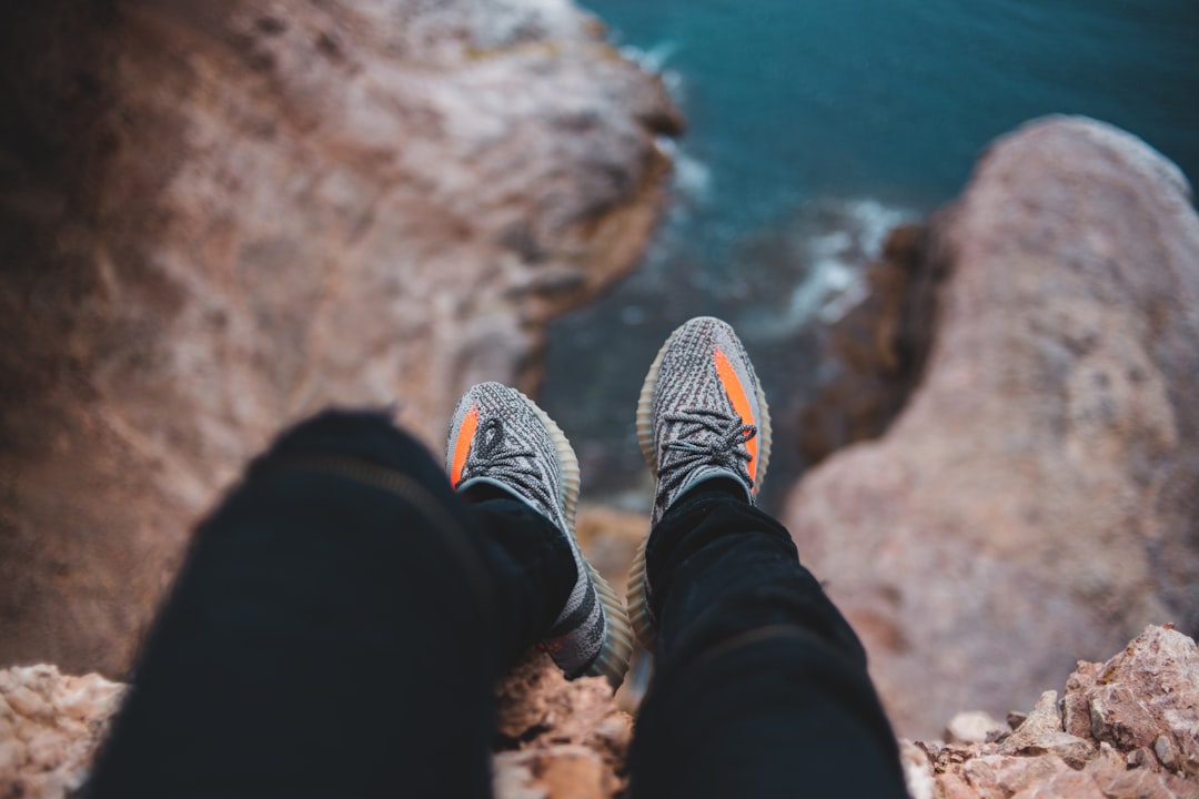 person in black pants and gray sneakers sitting on brown rock formation during daytime