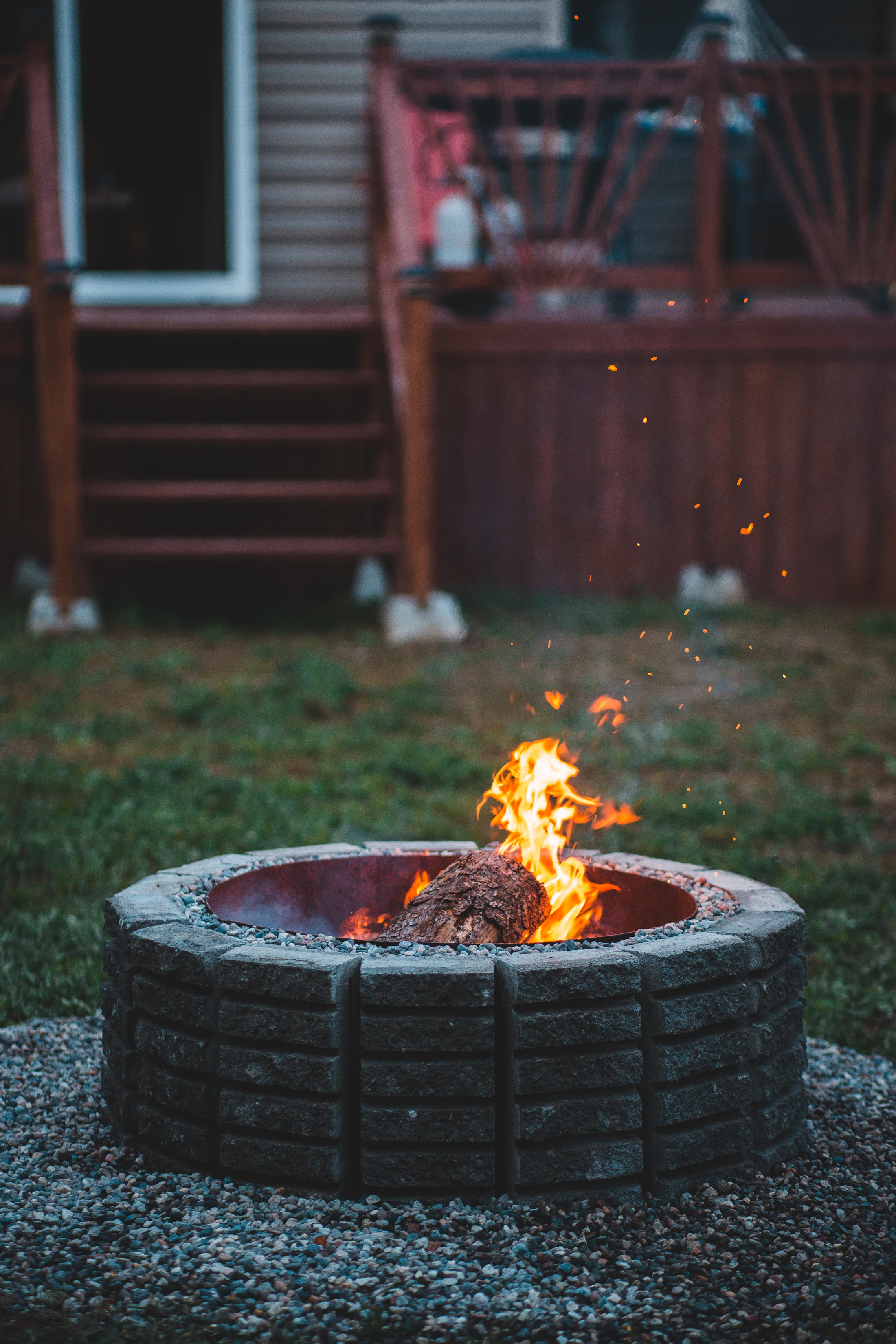 Round backyard fire pit with burning log and warm flames