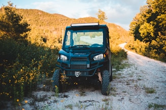 A rugged 4x4 vehicle parked on a scenic dirt road with lush green hills in the background.