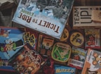 A collection of board game boxes with various designs and titles, including Ticket to Ride Europe, Top That!, and Beaver Gang. The games are stacked and arranged closely together, with colorful illustrations and text visible on the boxes. The setting suggests a playful and engaging environment, with hints of strategy and fun.