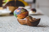 A vibrantly painted egg rests inside an intricately carved wooden shoe with floral designs, placed on a speckled countertop.