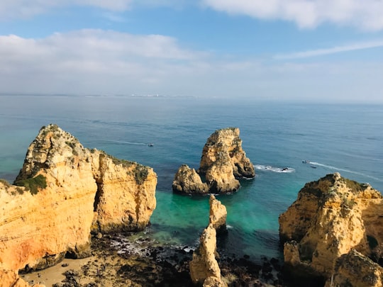 brown rock formation on sea under blue sky during daytime in Farol da Ponta da Piedade Portugal