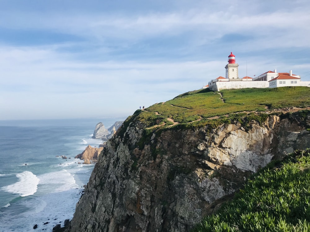 white and red lighthouse on brown and green mountain near body of water during daytime