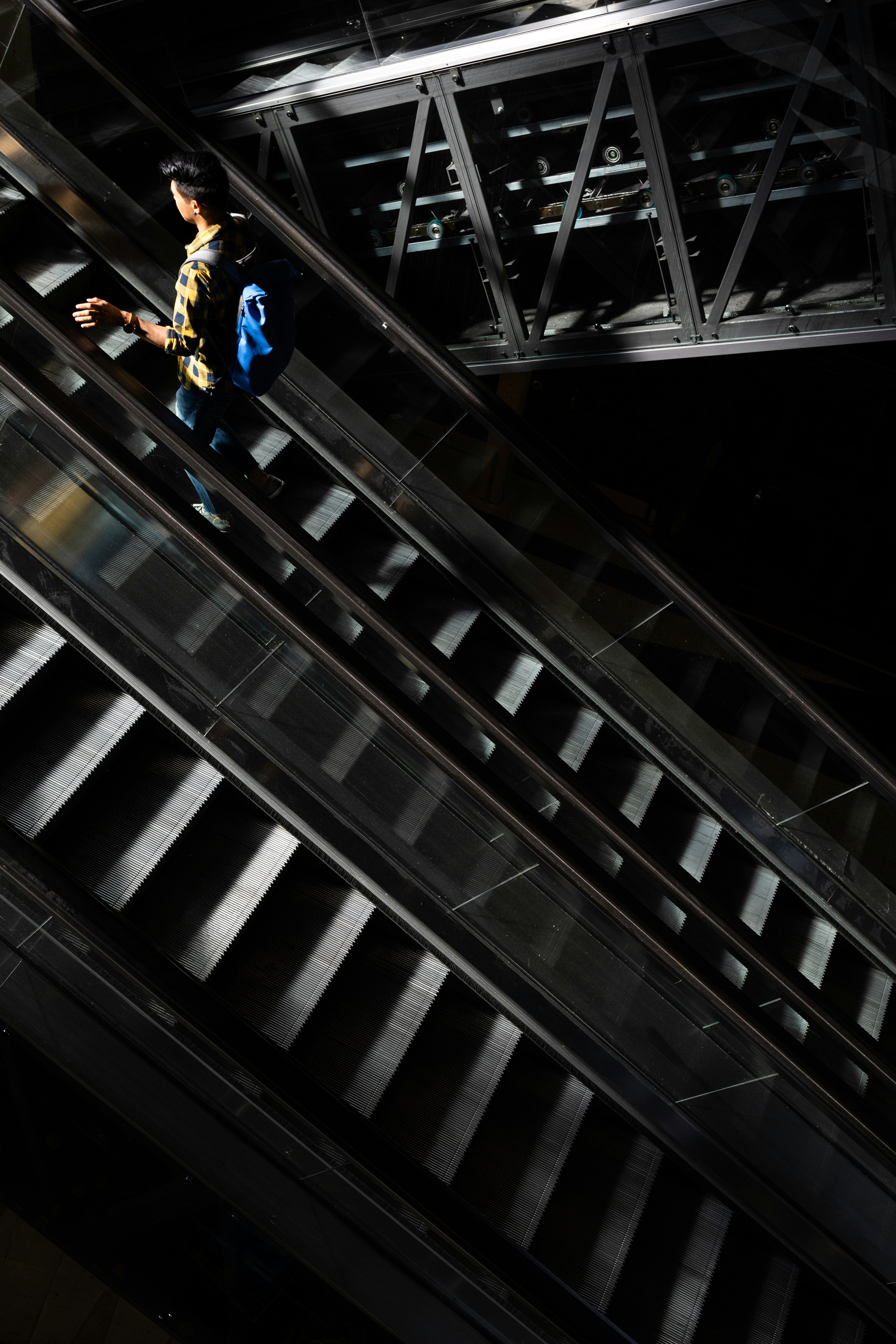 man in yellow jacket and blue denim jeans standing on escalator