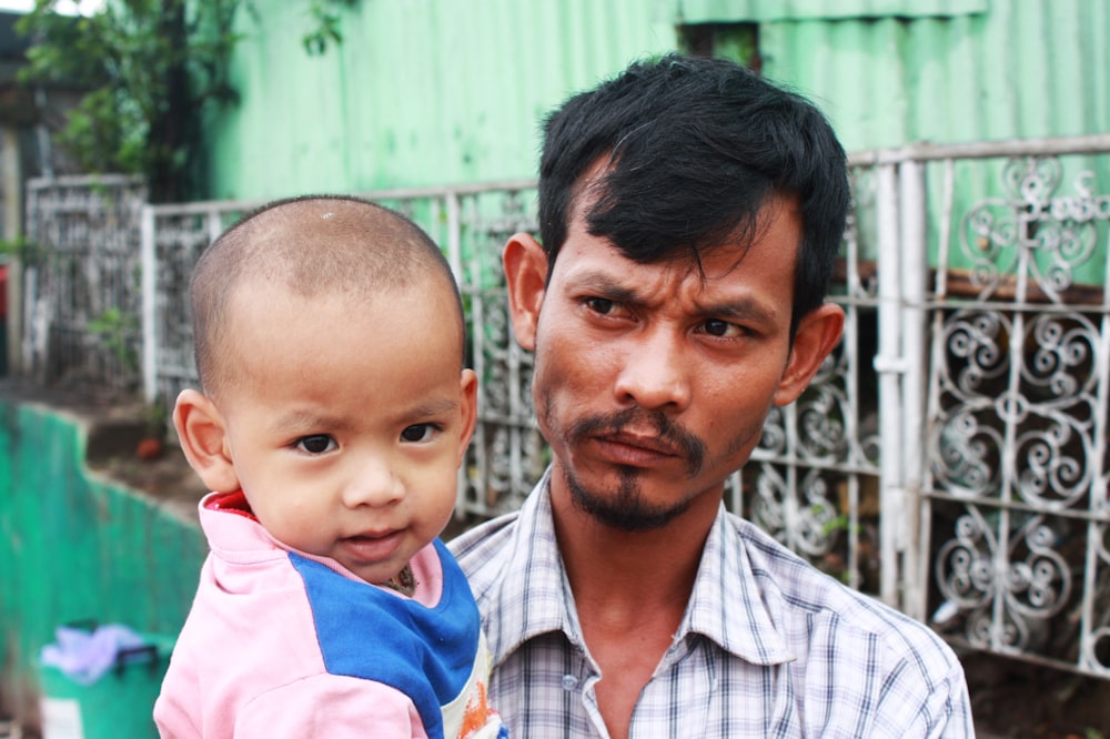 man in white and black plaid button up shirt carrying boy in pink polo shirt