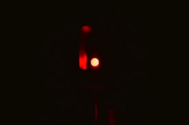 A single red traffic light is illuminated against a dark background, emitting a strong red glow.