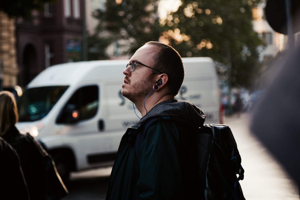 man in black jacket wearing eyeglasses standing near white car during daytime