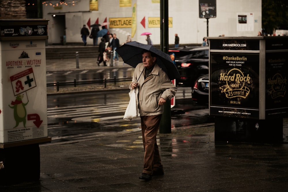 femme en manteau brun tenant un parapluie marchant sur le trottoir pendant la journée