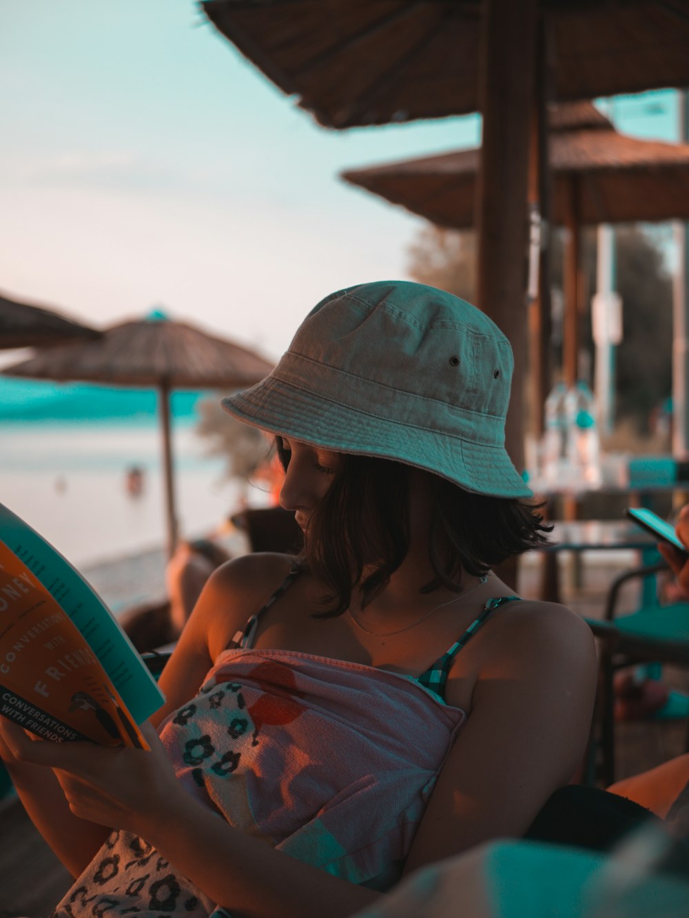 woman in blue and red floral tank top wearing blue hat sitting on chair during daytime