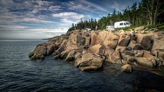 white and black boat on sea near brown rocky mountain under blue and white cloudy sky in Saint-Siméon Canada