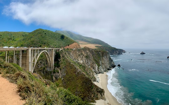 green and brown mountain beside body of water under blue sky during daytime in Bixby Creek Arch Bridge United States