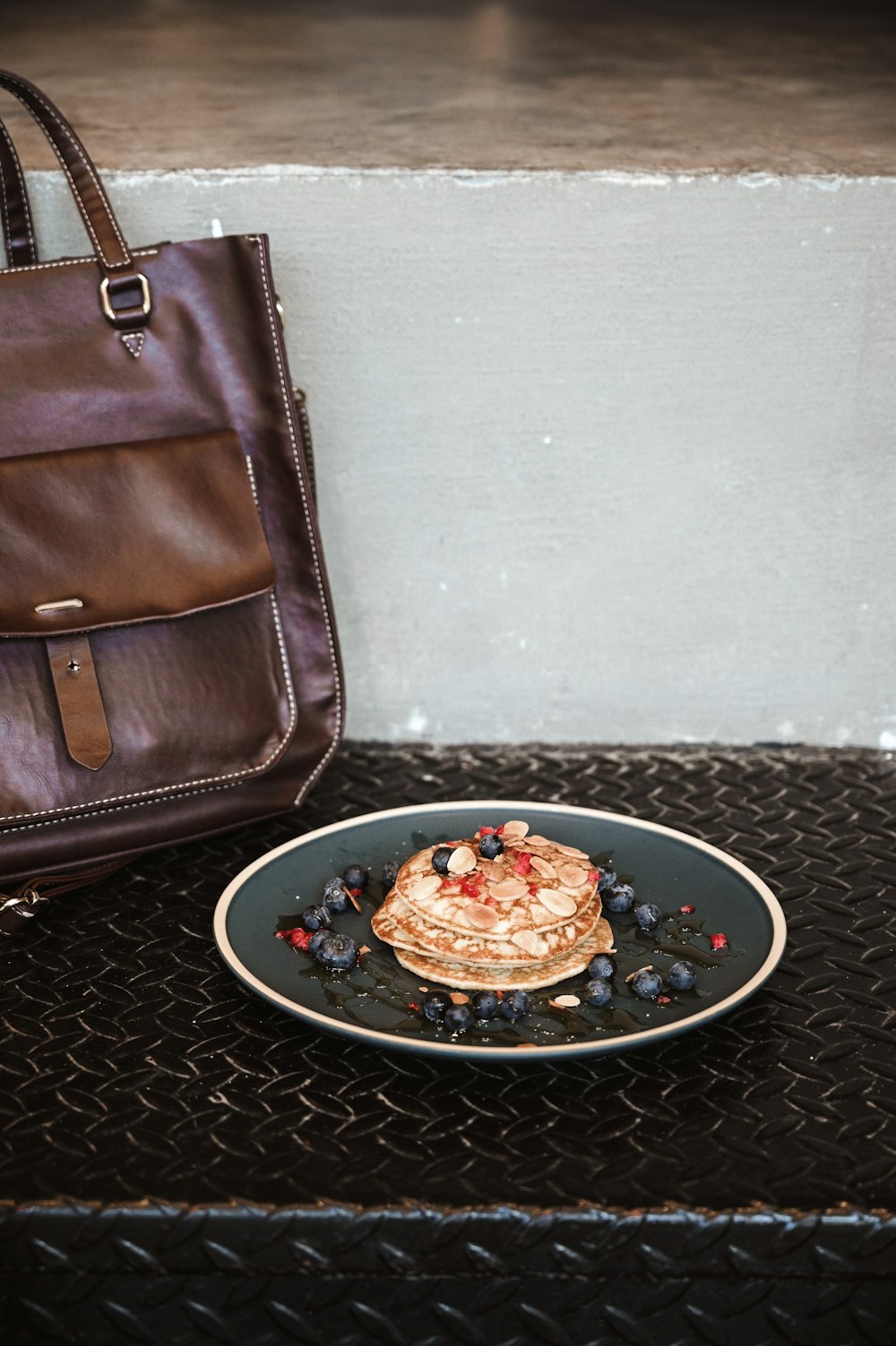 brown leather sling bag beside black round plate