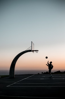 A basketball player dribbling on an outdoor court during sunset