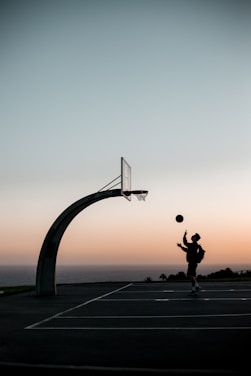 A coach guiding a focused young basketball player during an outdoor practice session at sunset.
