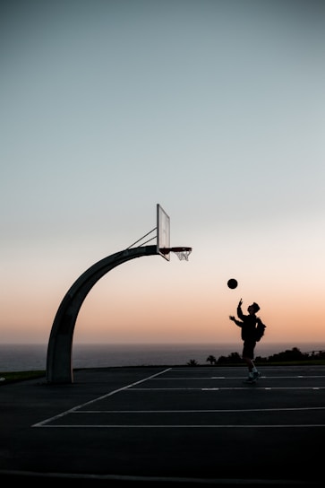 A coach guiding a focused young basketball player during an outdoor practice session at sunset.