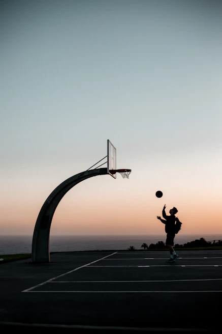 A college athlete performing intense dribbling drills on an outdoor court at sunset.