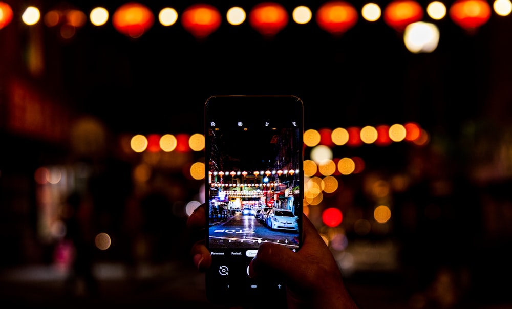 person holding black smartphone taking photo of city lights during night time