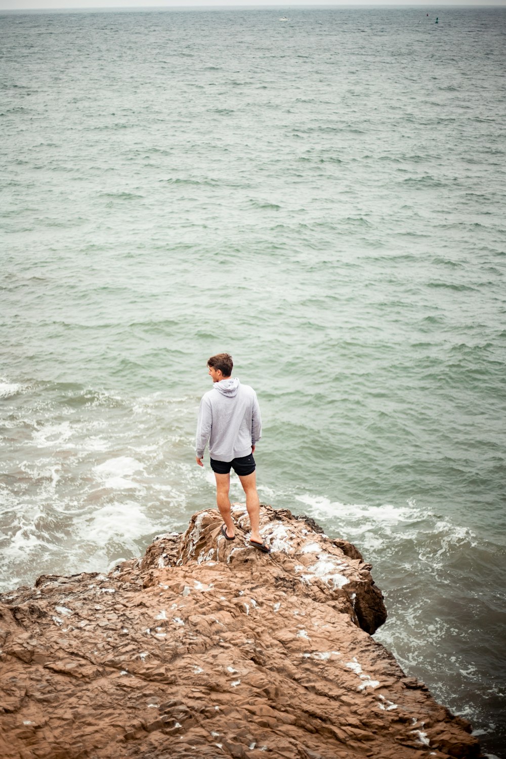 homem na camisa branca de pé na rocha marrom perto do corpo de água durante o dia