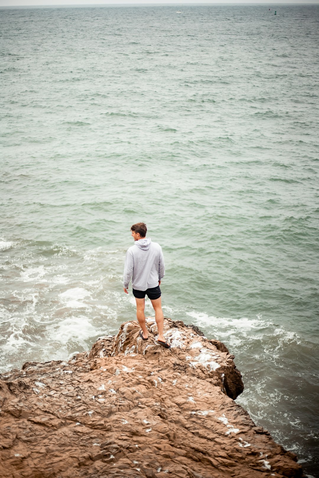 man in white shirt standing on brown rock near body of water during daytime
