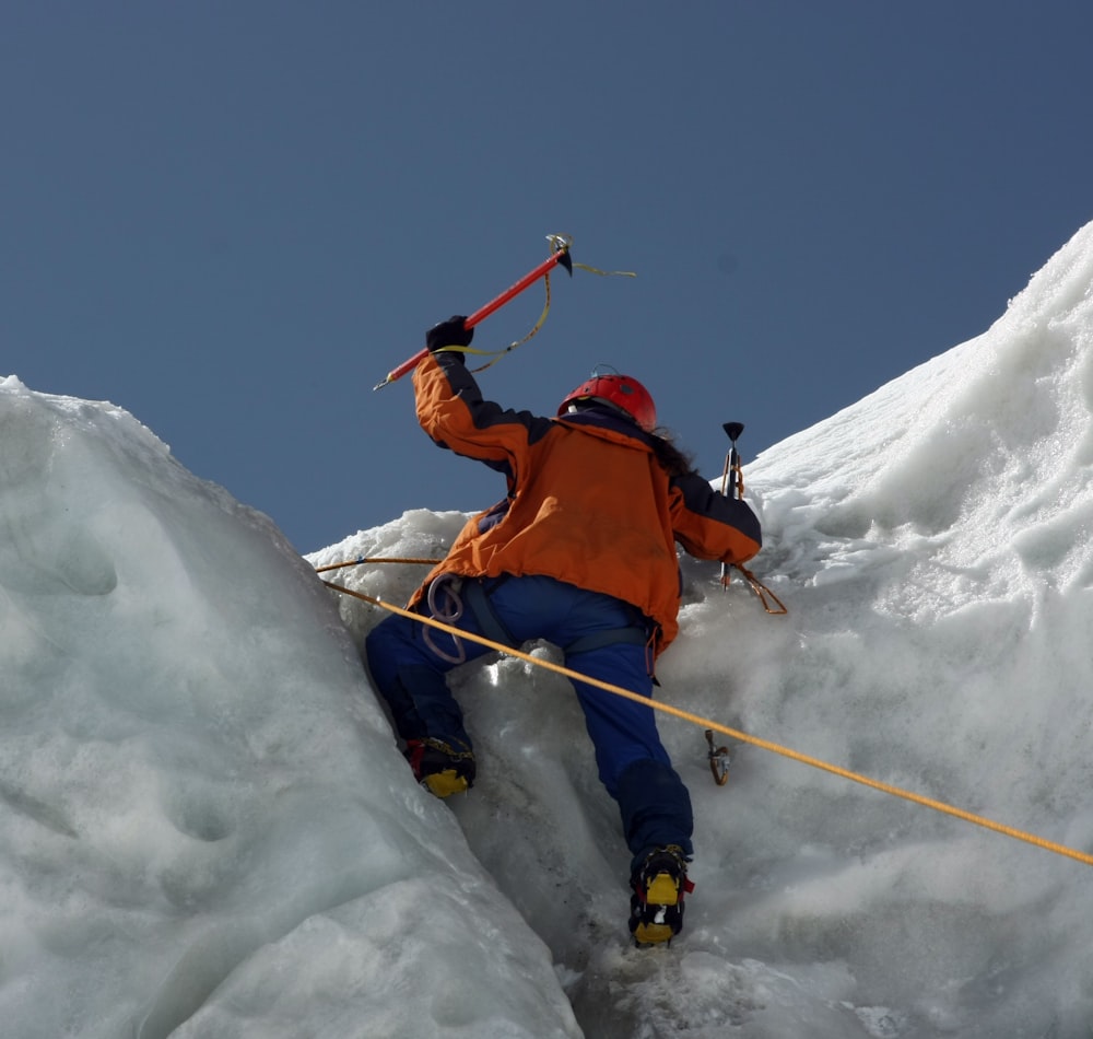 homme en veste orange et pantalon bleu sur la montagne enneigée pendant la journée