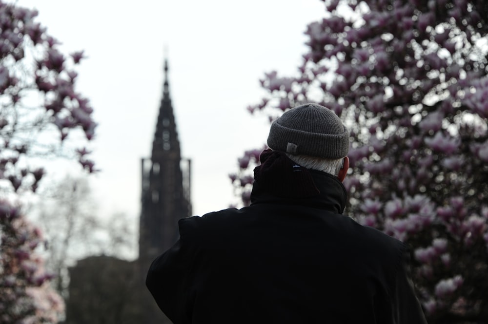 person in black jacket and gray knit cap standing near pink flower tree during daytime