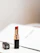 A close-up of a sleek black and gold lipstick tube resting on a deep red velvet fabric.