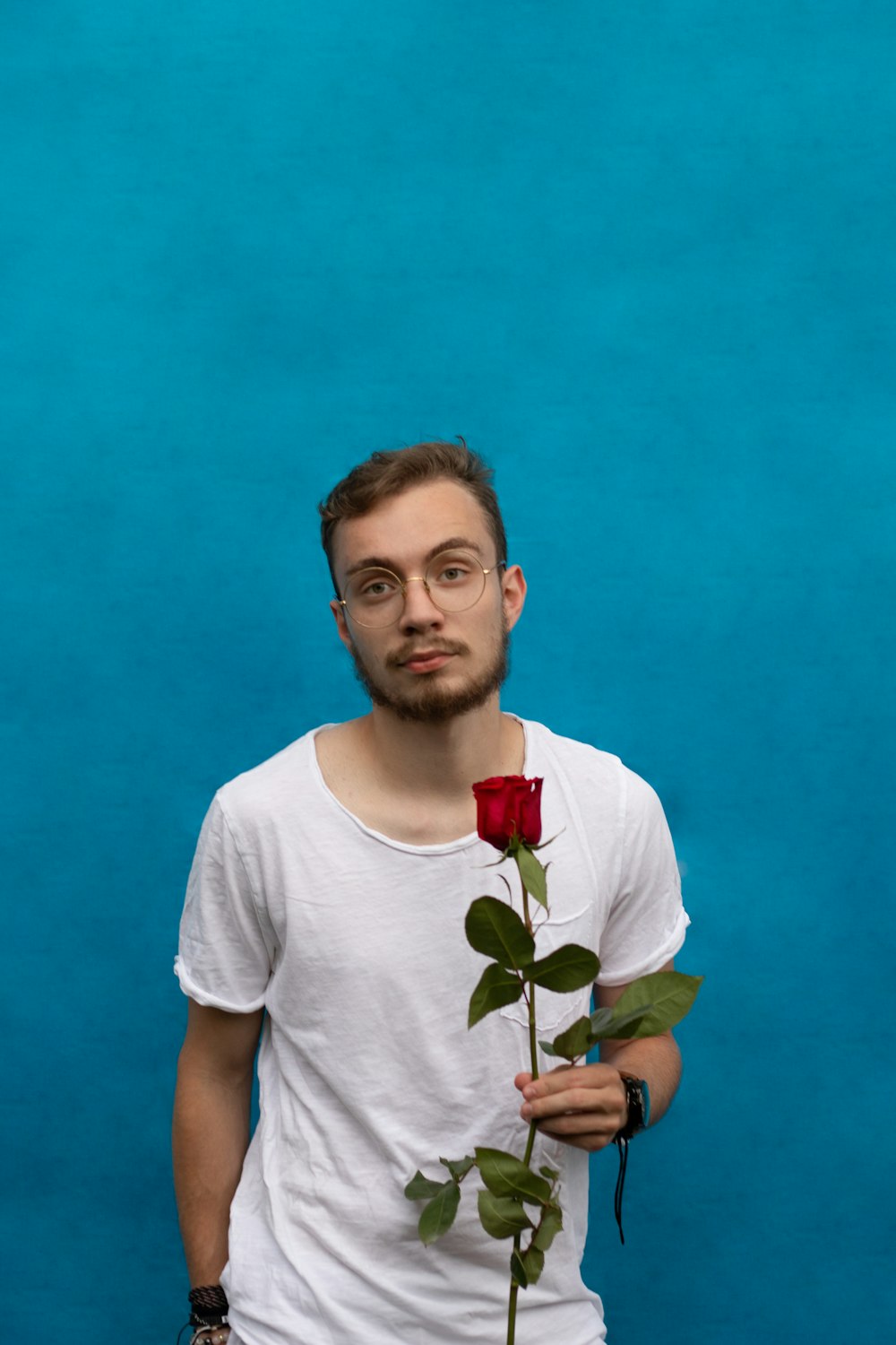 homme en t-shirt blanc à col rond tenant une rose rouge
