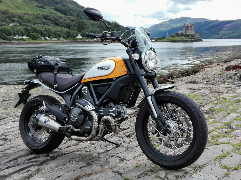 orange and black naked motorcycle on gray sand near body of water during daytime
