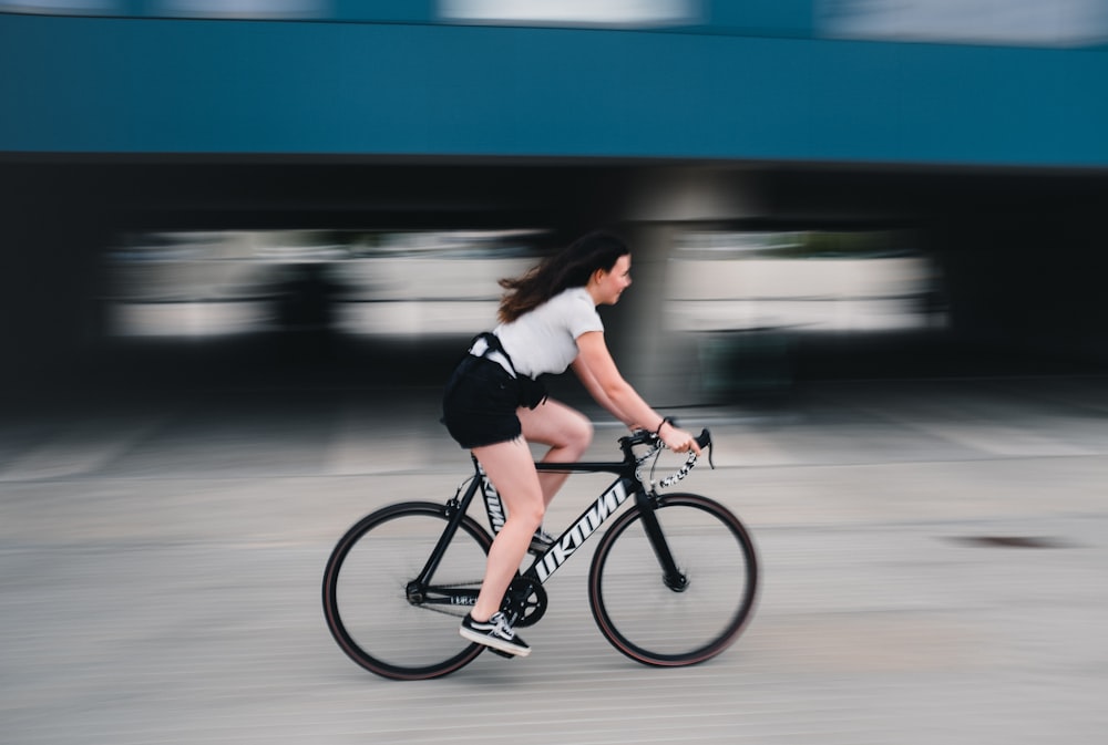 mulher na camisa preta e branca da manga comprida que monta a bicicleta preta
