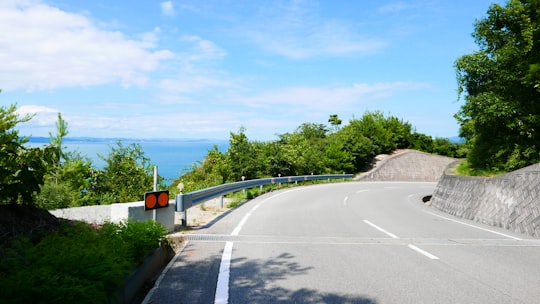 black and yellow road sign on gray asphalt road under blue sky during daytime in Teshima Japan