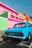 blue sedan parked beside pink and yellow painted building